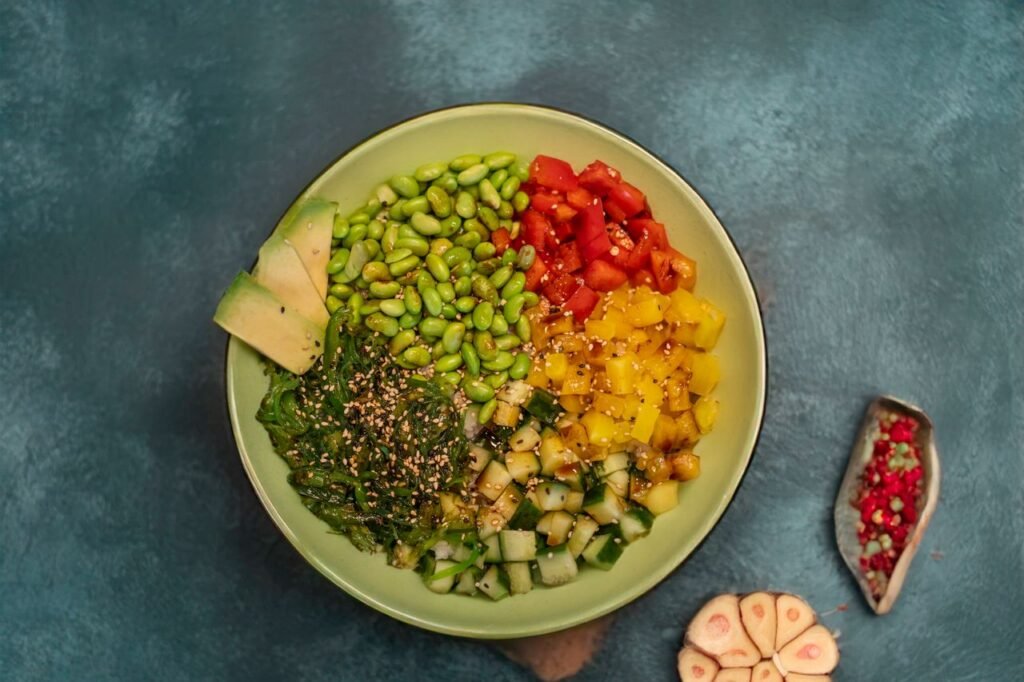 A colorful vegan poke bowl with fresh veggies, avocado, and spices on a textured blue background.
